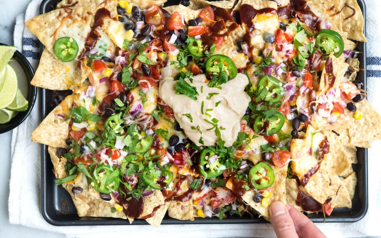 Tailgate food spread with loaded nachos, dips, wings, and veggies arranged on a table for game day.